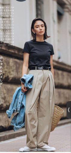 Woman in a black t-shirt and khaki pants holding a denim jacket and straw bag