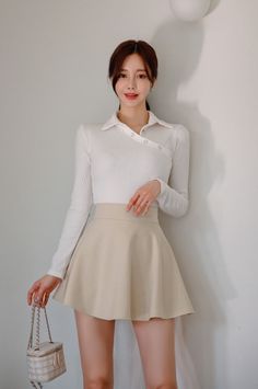 Woman in a white long sleeve shirt and beige mini skirt holding a small handbag