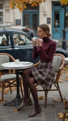 Woman in a turtleneck and plaid skirt drinking coffee at an outdoor cafe