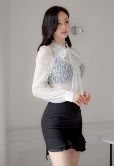 Woman in a white lace blouse and black mini skirt posing indoors