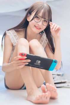 Woman with long hair and glasses holding a Nintendo Switch while sitting indoors