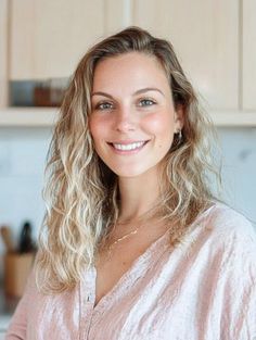 Woman with wavy blonde hair and a pink shirt smiling indoors