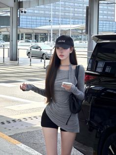 Woman in a grey top and black shorts wearing a baseball cap, holding a phone outdoors