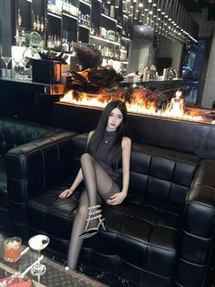 Woman with long black hair sitting on a black leather couch in a bar