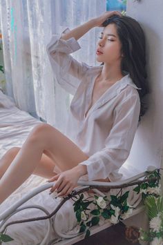 Woman in a sheer white shirt sitting on a bed with soft lighting