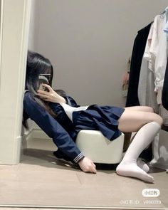 Person in a school uniform taking a mirror selfie while sitting on a stool