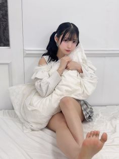 Woman with pigtails and a plaid skirt sitting on a bed with a pillow