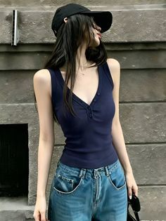 Woman with long hair wearing a black cap, navy tank top, and blue jeans outdoors