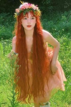 Woman with long red hair and a flower crown in a light pink dress standing in grass