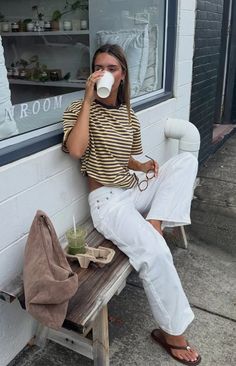 Woman in a striped t-shirt and white jeans sitting on a bench outdoors