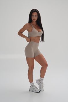 Woman in a beige sports bra and athletic shorts posing in a studio