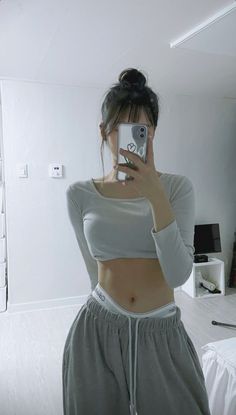Woman in a crop top and sweatpants taking a mirror selfie