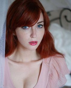 Woman with red hair and blue eyes in a pink top, looking at the camera
