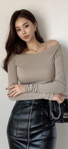 Woman with long hair wearing an off-shoulder top and leather skirt, holding a quilted bag