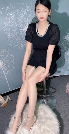 Woman in shiny pantyhose, black top, and shorts sitting on a stool