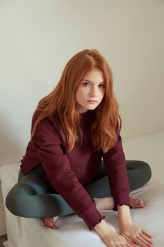 Young woman with long red hair wearing a burgundy sweatshirt and green leggings