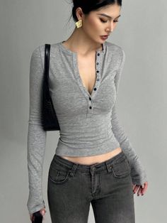 Woman in a gray long sleeve shirt and low rise jeans with a black handbag