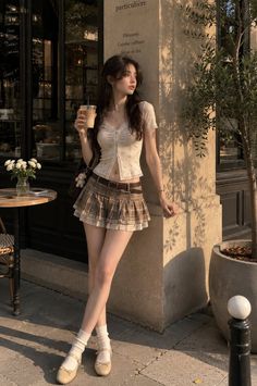 Woman in a plaid skirt and crop top holding a drink outdoors