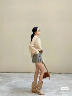 Woman in an oversized sweater, pleated skirt, and cowboy boots with a shoulder bag