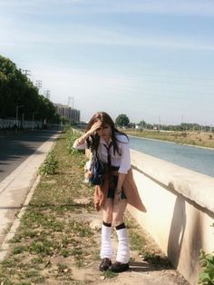 Person in a school uniform with leg warmers standing by a river on a sunny day