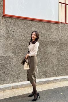 Woman in a cream top and olive midi skirt holding a handbag outdoors