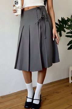 Person in a gray pleated skirt and white crop top holding a phone