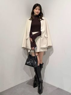 Woman in a blazer, mini skirt, and knee-high boots holding a black handbag