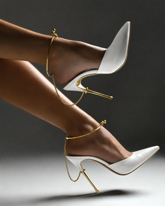 Pair of white high heels with gold chain anklets on a dark background