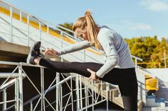 Woman in athletic wear stretching her leg on a railing outdoors