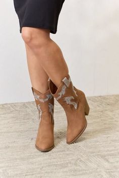 Person wearing brown cowboy boots with sparkly details and a short black dress