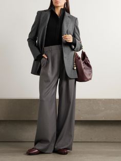 Woman in a gray blazer and wide-leg pants holding a burgundy bag