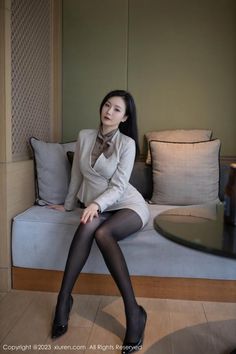 Woman in a business suit and black pantyhose sitting on a couch indoors