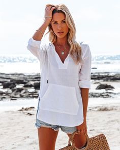 Woman with blonde hair in a white hoodie and denim shorts on a beach