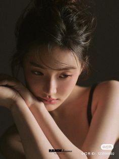 Woman with dark hair in an updo wearing a black bra, looking down