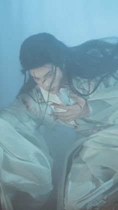 Person in a white robe with blood stains and long dark hair