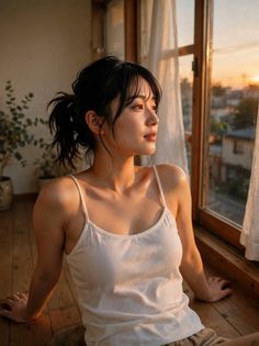 Woman in a white tank top sitting by a window at golden hour