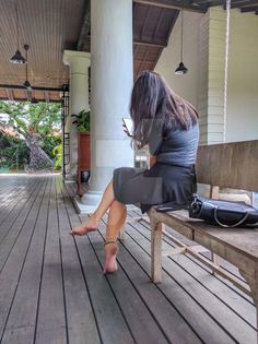 Woman with long hair sitting barefoot on a wooden bench outdoors