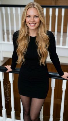 Woman with long blonde hair and freckles in a black dress, smiling indoors