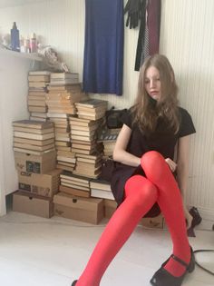Young woman with long hair wearing a black dress and red tights, sitting on the floor