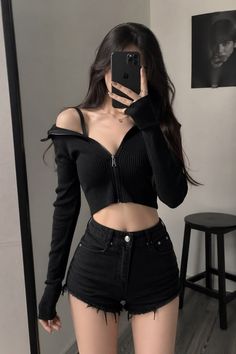 Woman in a black crop top and denim shorts taking a mirror selfie