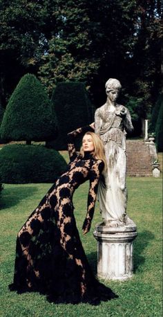 Woman in a black lace dress posing next to a statue in a garden