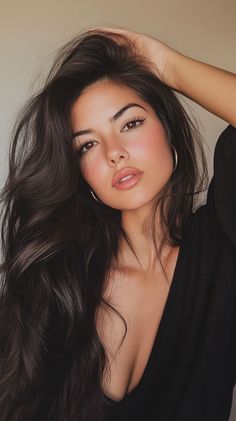 Woman with long dark hair and hoop earrings in a black top with cleavage