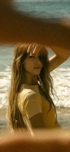 Woman with long hair on a beach, shielding her eyes from the sun