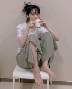 Woman with black hair in a messy bun, sitting on a chair and drinking from a mug