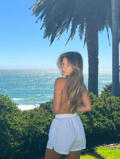 Woman with long hair in white shorts looking over her shoulder at the beach