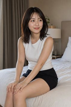 Woman with short dark hair sitting on a bed in a white tank top and black shorts