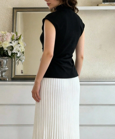 Woman in a black top and white pleated skirt, seen from behind indoors