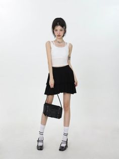 Woman in a white tank top and black mini skirt holding a shoulder bag