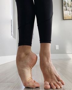 Person in black leggings standing on a wooden floor, one foot en pointe