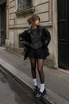 Woman in a leather jacket and pleated skirt on a city street